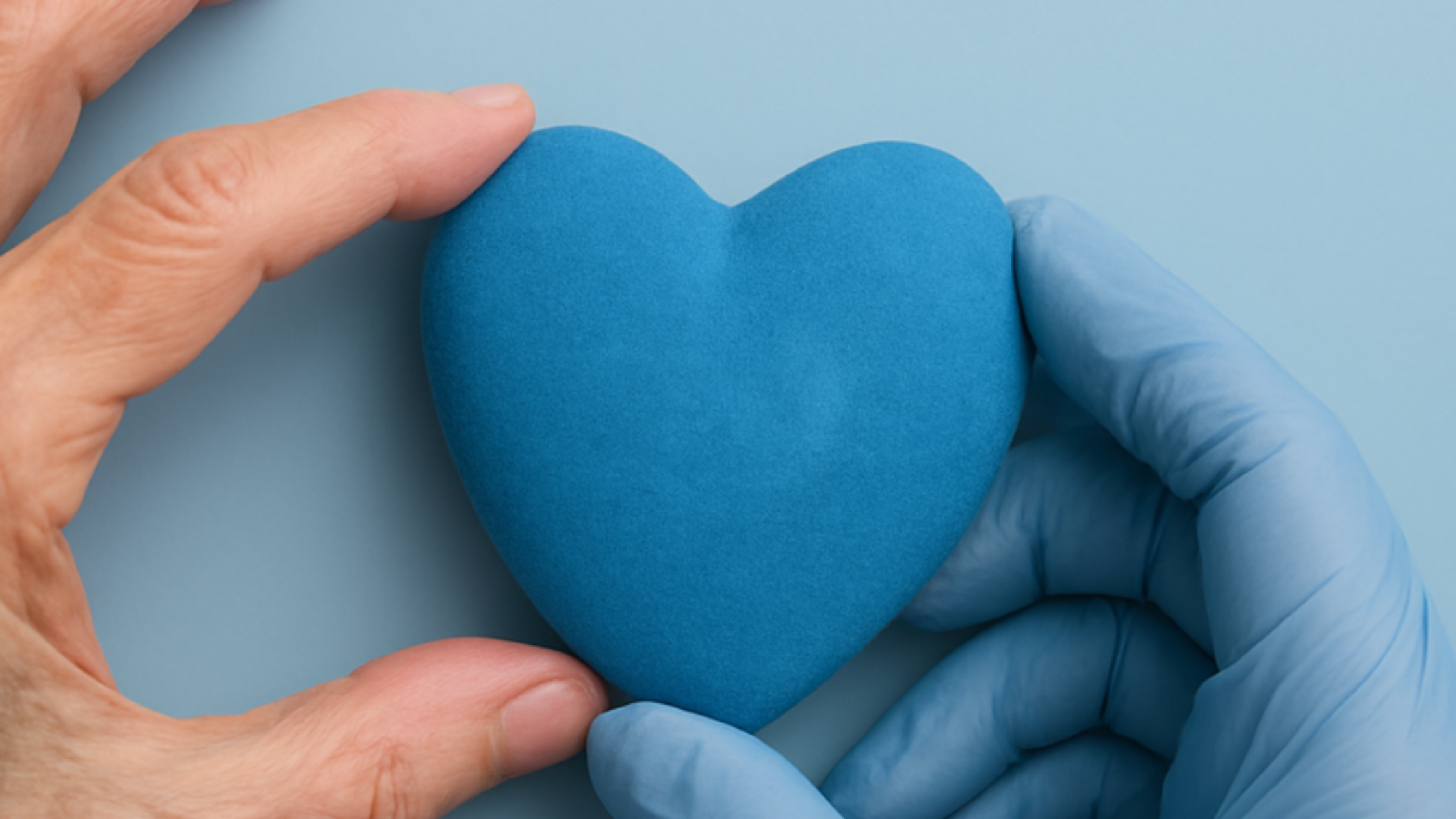 Dos manos sostienen un corazón azul de fieltro sujetándolo con el pulgar y el índice. Una de las manos lleva guantes de vinilo azul