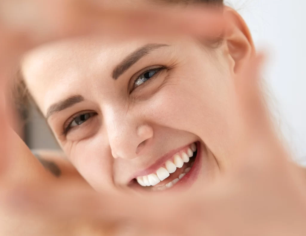Primer plano de mujer sonriente que enmarca su rostro con las manos, mostrando dientes blancos y expresión alegre