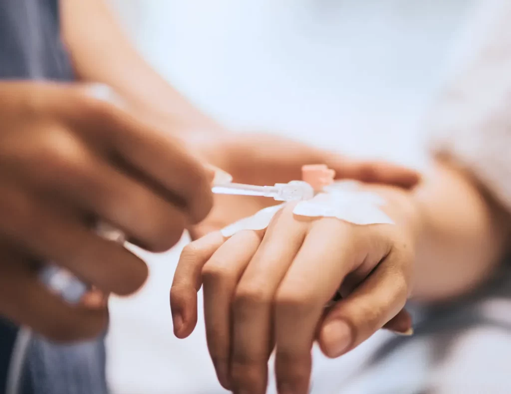 Mano de una paciente con vía intravenosa siendo colocada cuidadosamente por un profesional, como parte del proceso de sedación consciente.